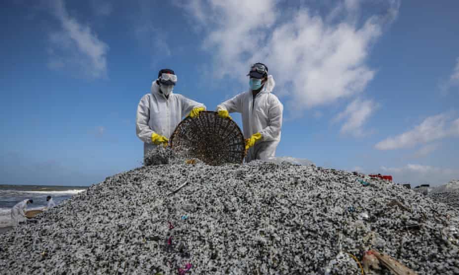 Sri Lankan navy personnel in protective clothing empty baskets of plastic pellets on to a big pile on a beach