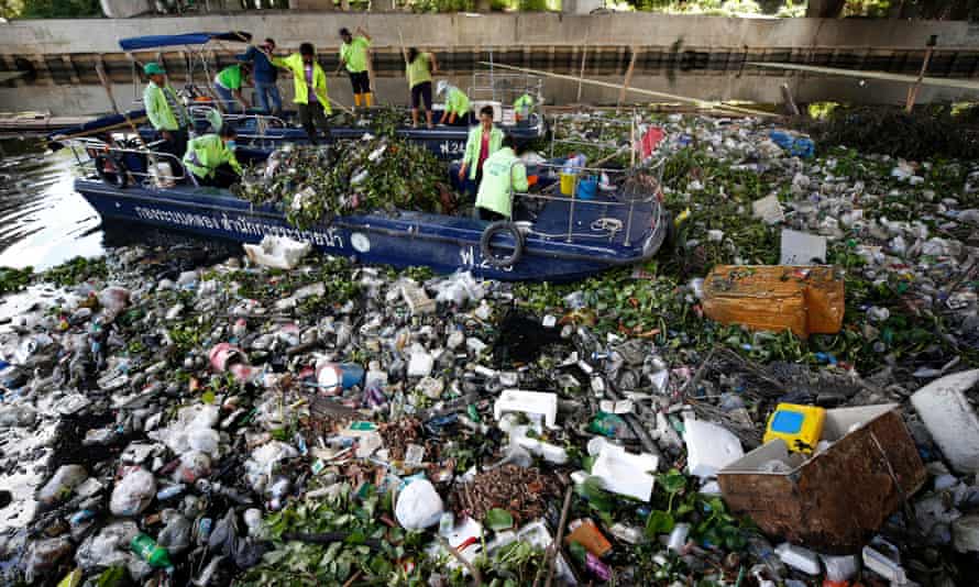 Municipal rubbish collectors in boats try to  clear a canal of flotsam and household waste