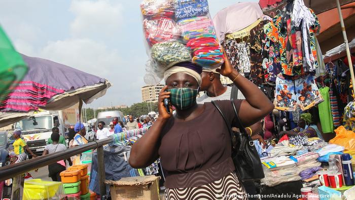 A woman carries six piles of linen on her head at the market while speaking on a mobile phone