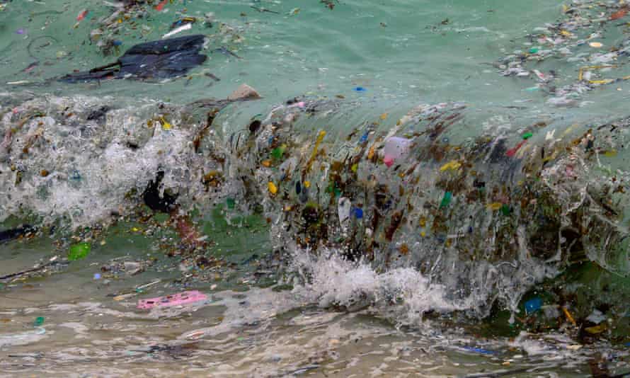 A wave full of plastic waste breaks on a beach