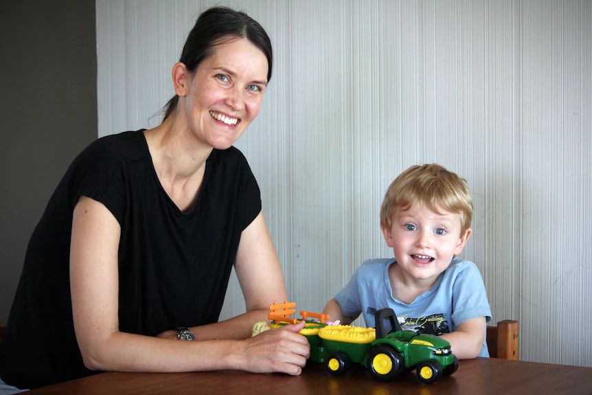 A mother and young son sit at a table and smile while playing with a toy truck
