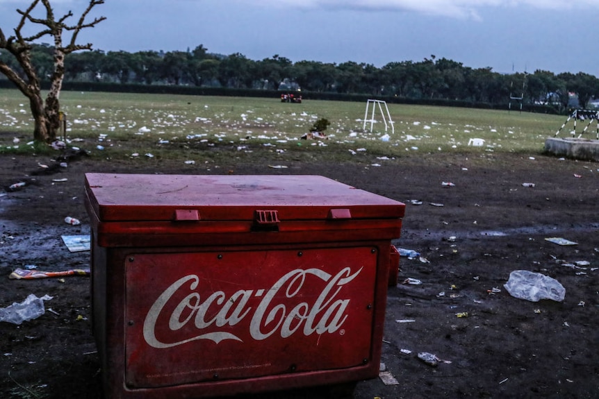 A Coca Cola esky surrounded by rubbish.