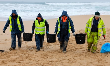People in high vis jackets carrying buckets on beach